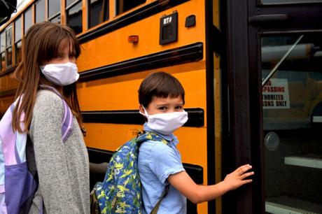 Deux enfants montent à bord d'un autobus scolaire tout en portant des masques faciaux.