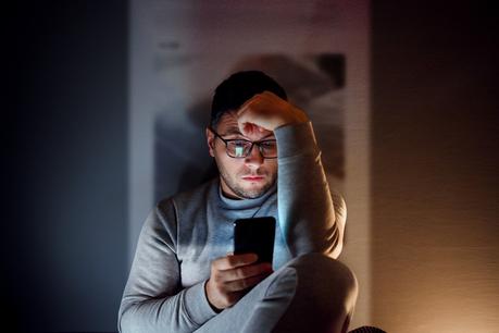 Un homme assis dans une pièce sombre, utilisant son smartphone.