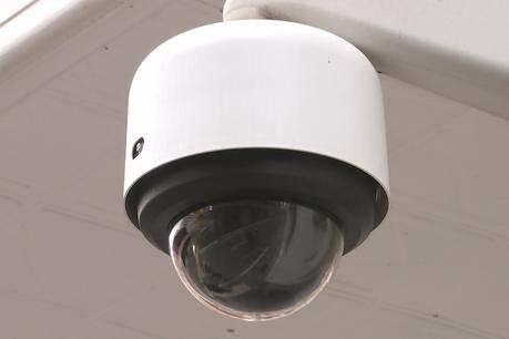 Une sphère noire émerge de la base d'un cylindre blanc monté au coin d'un mur