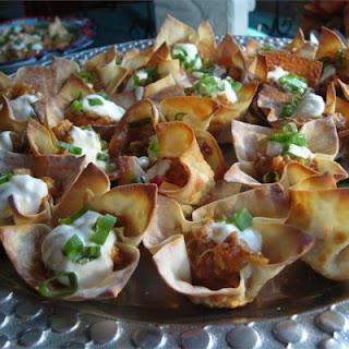 Cups made from wonton wrappers are filled with a flavorful cheese and sausage mixture, then baked and topped with sour cream and chopped green onions.