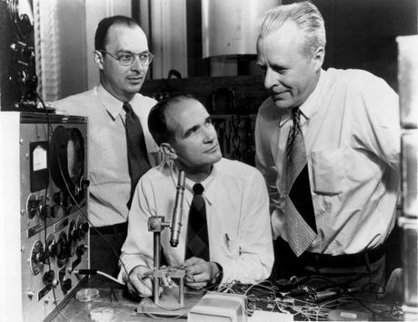 Trois physiciens en chemise et cravate dans les laboratoires Bell en 1948. Il y a un microscope au milieu de la photo pointé sur un transistor.