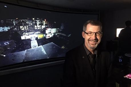 Le Dr Mark Dunn est assis dans une pièce sombre devant un écran de réalité virtuelle montrant une mine de charbon souterraine.