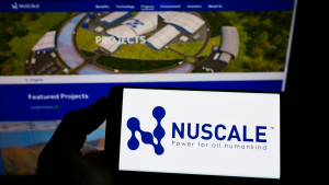 Une main en silhouette tient un téléphone affichant le logo de Nuscale devant un écran affichant le site Web de l'entreprise.
