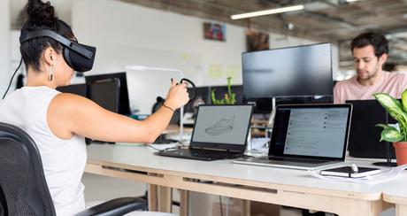 Femme portant un casque VR au bureau avec des ordinateurs sur la table